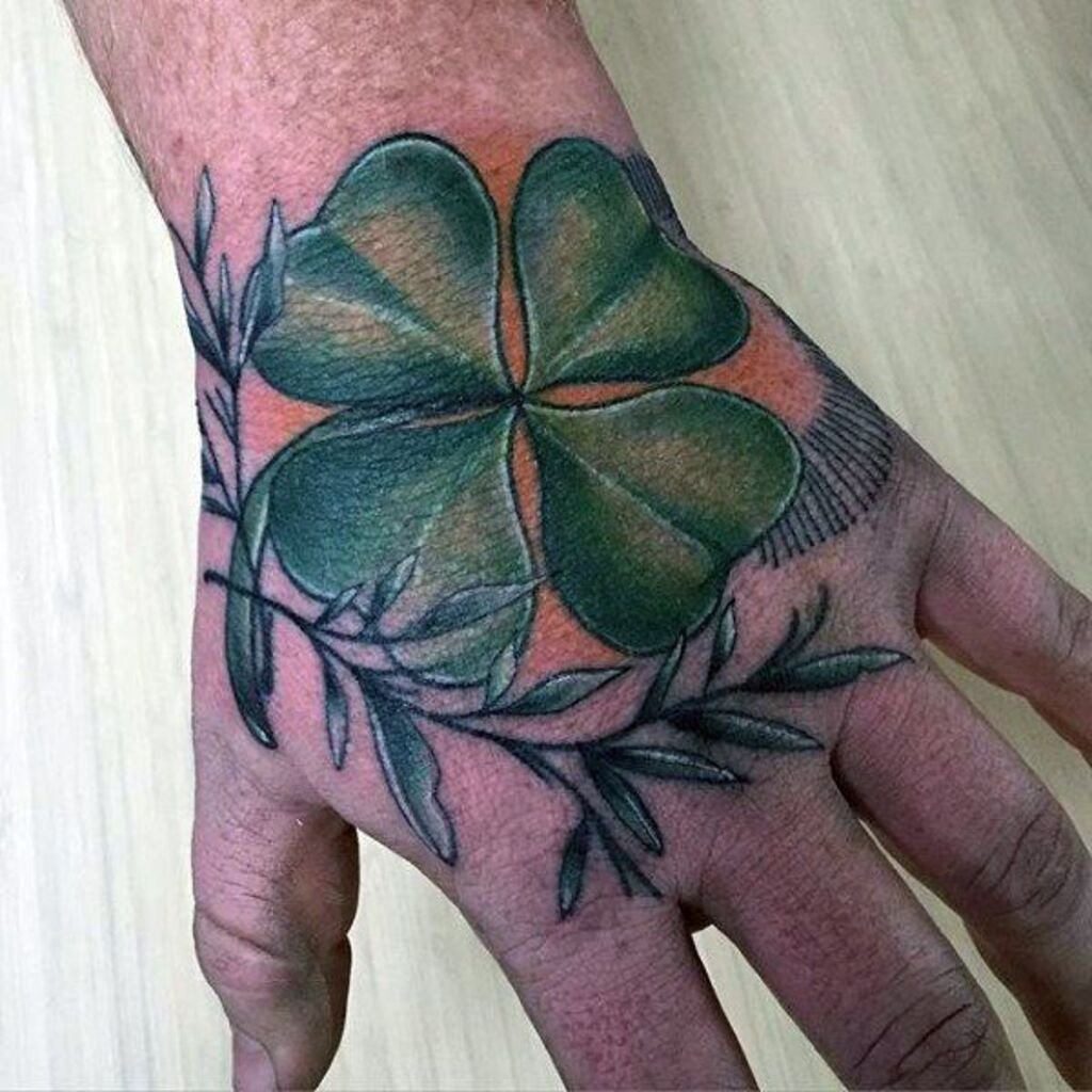 Small, fine-line tattoo of a four-leaf clover on a man's hand