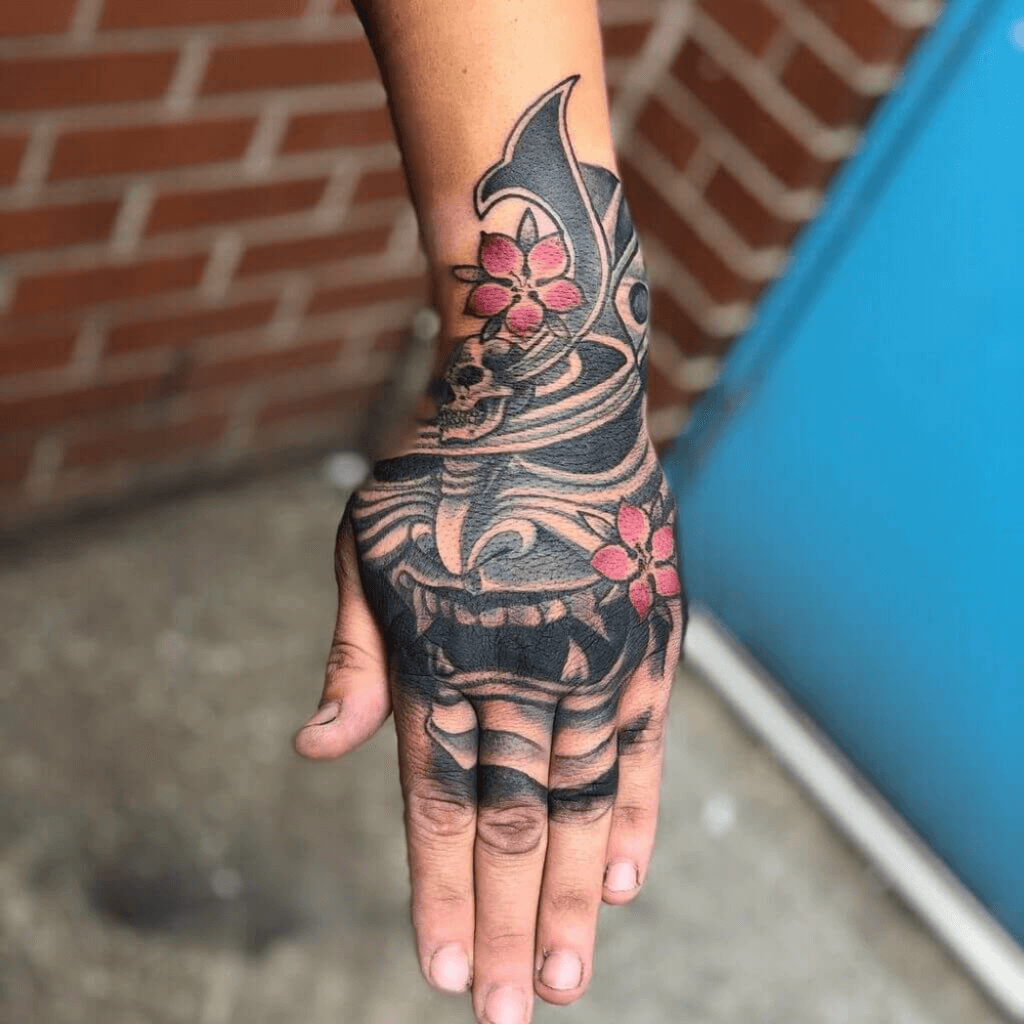 A man's hand has a tattoo of a grim vase design.